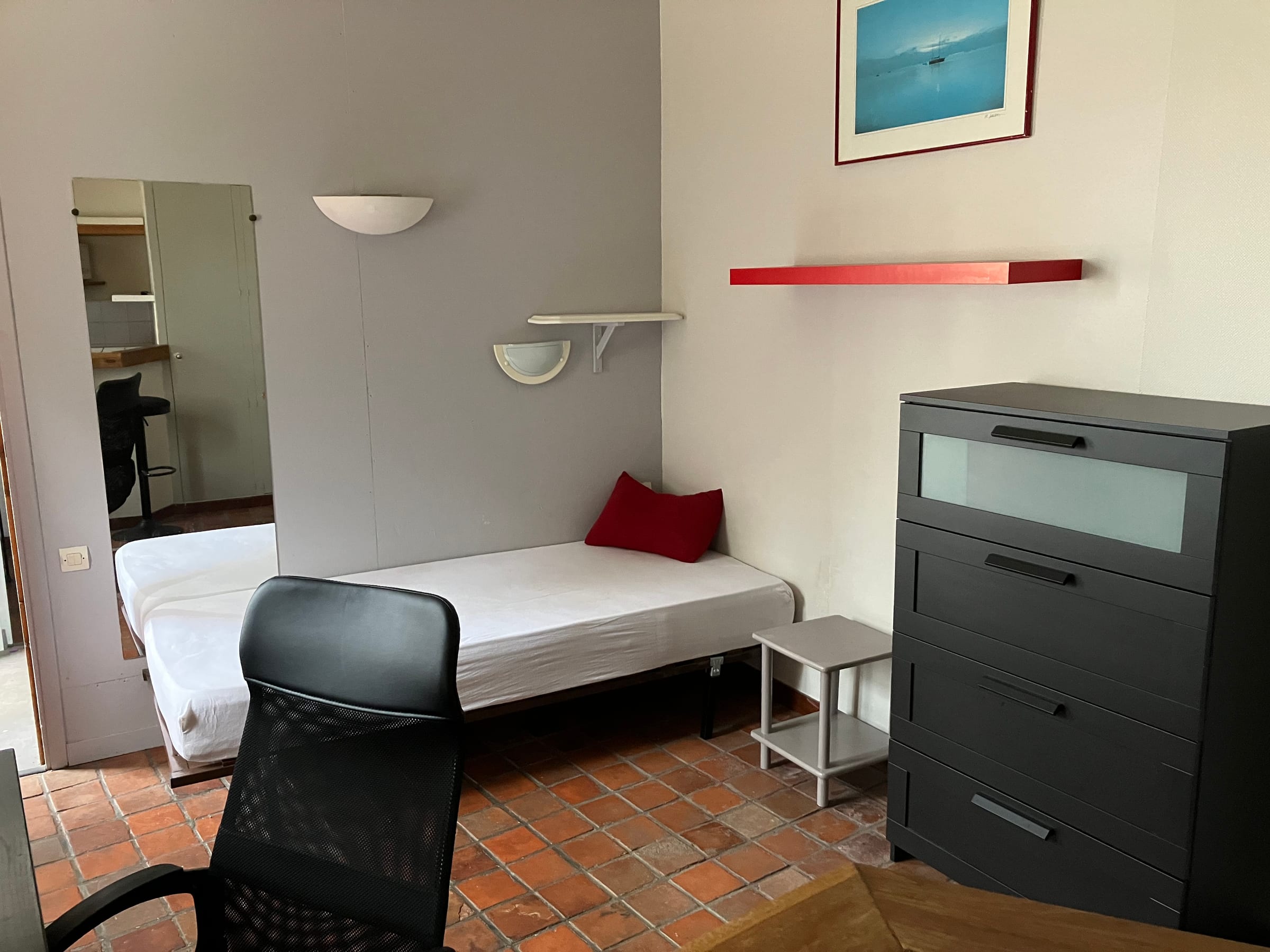 Coin nuit du studio avec lit, commode et miroir